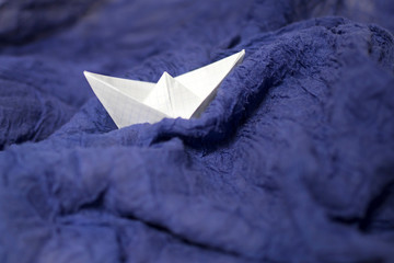 Paper checkered boat on blue draped fabric symbolizing the waves and the storm