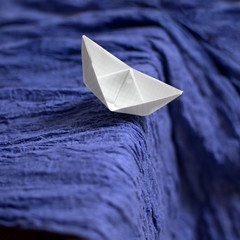 Paper checkered boat on blue draped fabric symbolizing the waves and the storm