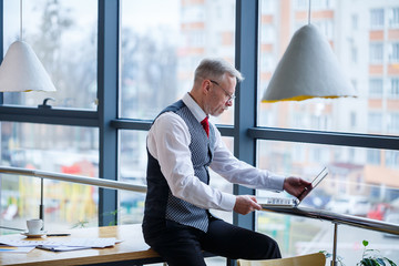 Adult male businessman, teacher, mentor working on a new project. Sits by a large window on the...