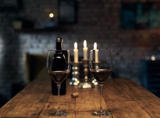 Two glasses of red wine on wooden table at home. Romantic mood, warm colors, candle light dinner. Brick wall in the background.