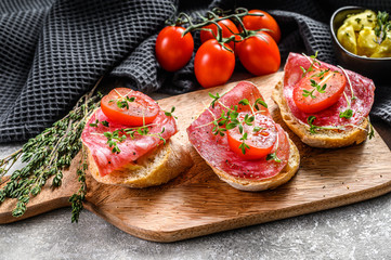 Open baguette sandwich with salami salchichon, cherry tomatoes and micro greens. gray background. top view