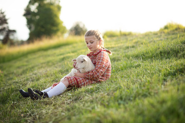 cute little girl holding spring newborn lamb sheep on a green grass farm field 