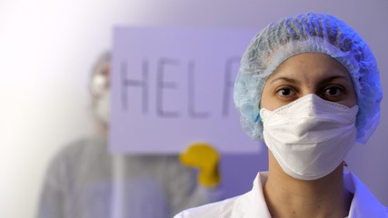 Fototapeta na wymiar Portrait of a female doctor in medical mask, white lab coat. Man in a protective surgical suit, safety glasses, and protective medical mask holds a sign saying 