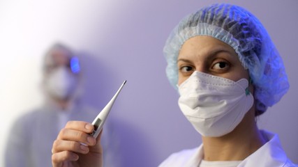 Portrait of woman doctor or nurse in a protective medical mask shows a thermometer in her hands. Coronavirus or COVID-19.