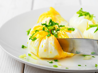 Eggs - poached decorated with fresh herbs on a white plate, close-up, shallow depth of field. A knife cuts an egg. The idea of making a healthy breakfast or lunch with organic products.