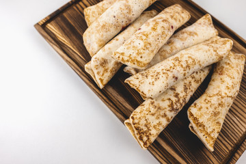 Frozen stuffed pancakes on a wooden board isolated on white background.