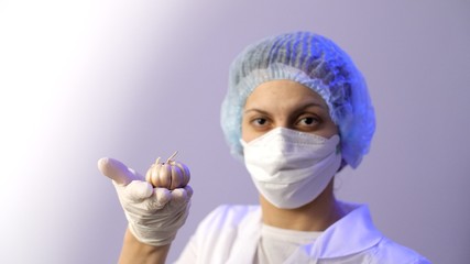Cute female doctor in a medical protective mask holds garlic in hands. Coronavirus or COVID-19. Useful products for immunity