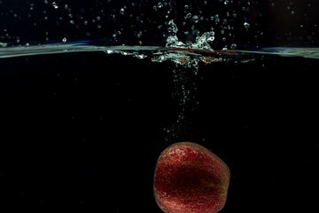 Close up view of colorful apple falling in water on black background.  Gorgeous backgrounds.