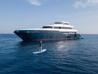 Girl on paddle board close to a luxury yacht