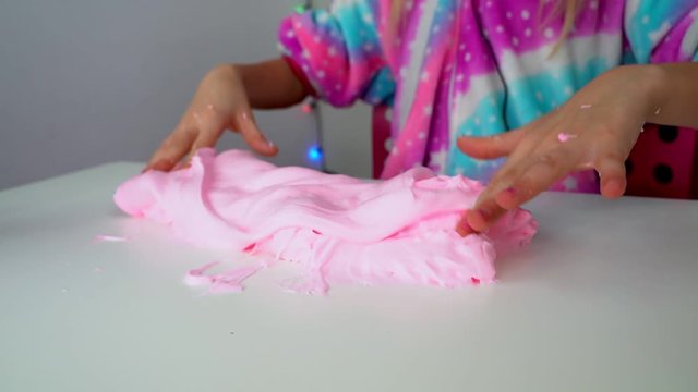 The girl hands make a large pink slime in a bowl on a white table.