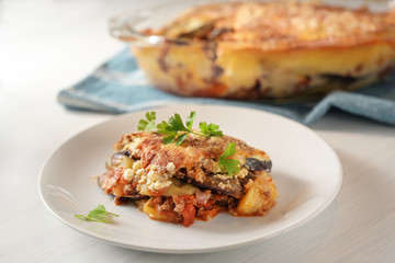 Fototapeta premium Moussaka, traditional Greek baked casserole of eggplants, potatoes, minced meat and tomatoes served with parsley garnish on a plate on a white table
