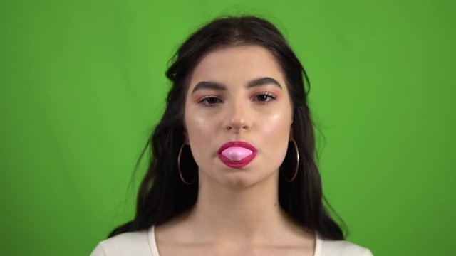 Funny girl blowing giant bubble gum on green screen slow motion