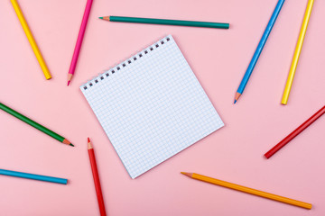 notebook on a pink background. Colored pencils are scattered nearby.