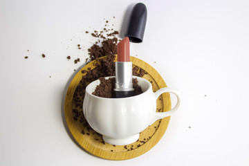 Lipstick inside of cup of coffee beans coffee beans around on white background, makeup concept.