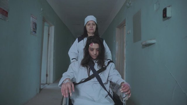 Female Nurse Pushing Patient In The Wheelchair Through The Hospital Corridor
