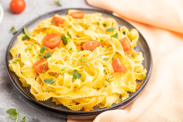 Reginelle semolina pasta with tomato, eggs and microgreen sprouts on a gray concrete background. Side view, selective focus.