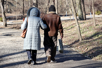 Elderly woman and man with bag walking down the street, rear view. Old couple in warm clothes in spring park during the quarantine of covid-19 coronavirus pandemic