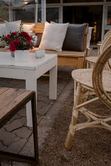 Decoracion de sala de estar con sillas de mimbre, mubles de madera, velas, flores rojas y almohadones blancos.