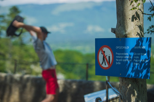 Man throwing an object over a fence despite the warning sign or board prohibiting throwing rocks. Reckless or ignorant behavior of visitors in nature.