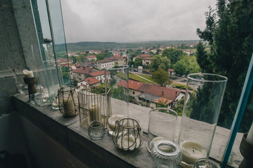 Panorama of the city of Stanjel in Slovenia on a cloudy spring day, looking through window with a collections of candles in the foreground