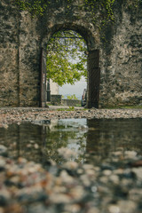 View towards the entrance with arch made of rock and marble on a terrace in the village of Stanjel, Slovenia on a romantic rainy day with a reflection seen on the gravel floor.
