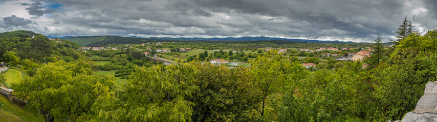 Fototapeta na wymiar Panoramic view from the village of Stanjel, Slovenia towards Nanos massive, on a cold cloudy spring day with dense clouds covering the sky.