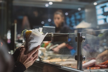 Person holding a fresh kebab or gyros in his hands in front of a fast food vendor or stall. Kebab...