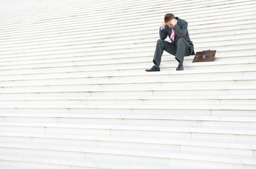 Depressed businessman sitting outdoors on a large white staircase hanging his head in his hands