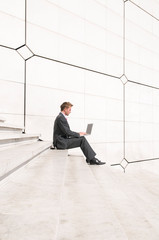 Businessman sitting outdoors on minimalist marble steps using his laptop computer 