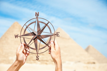 Hands holding up a traditional compass rose in desert sun against background of. the Great Pyramids in Egypt