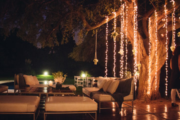 Decoracion de jardin con luces, plantas y sillones de madera.