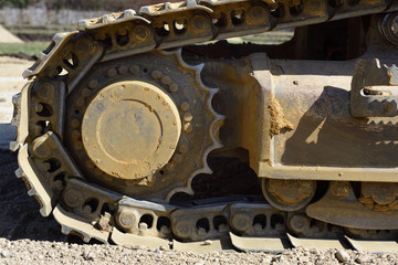 Fototapeta na wymiar Detail and close-up of the metal wheels and the wheel chain of an excavator on a construction site with soil and dirt