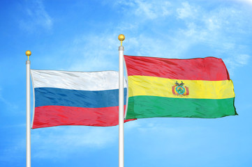 Russia and Bolivia  two flags on flagpoles and blue cloudy sky