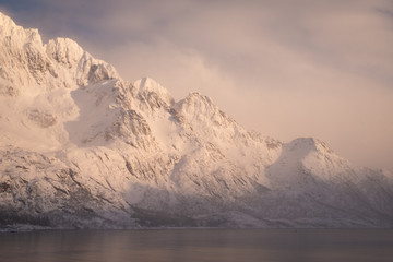 Fototapeta na wymiar peaks of norway in lofoten islands. near to svolvaer town. ambient light after heavy snow in the fjord. soft light and very calm atmosphere. clouds and fog making the right vibe of the picture