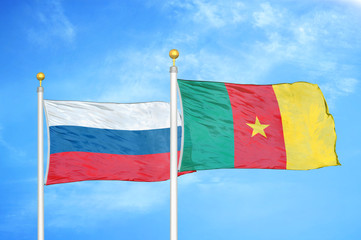 Russia and Cameroon  two flags on flagpoles and blue cloudy sky