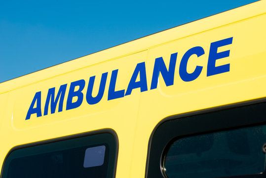 Ambulance sign on the side of NHS medical response vehicle, against a clear blue sky.