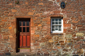 Red medieval wall with wooden door and fortified window. Campbeltown street, Scotland.