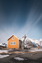 famous yellow cabin with olstind mountain in lofoten islands near to reine town on sakrisøy island. typical lofoten spot for tourist and photography. winter norway. nice blue sky with motion clouds. 