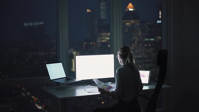 Female trader searching online offers for making new profitable money investment using blank monitor with copy space area for financial website, young woman having extra hours in office workspace
