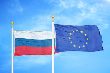 Russia and European Union two flags on flagpoles and blue cloudy sky