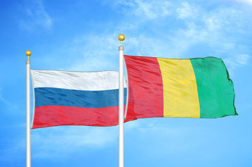 Russia and Guinea two flags on flagpoles and blue cloudy sky