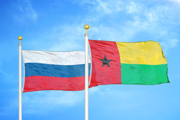 Russia and Guinea-Bissau two flags on flagpoles and blue cloudy sky