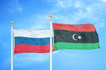 Russia and Libya two flags on flagpoles and blue cloudy sky