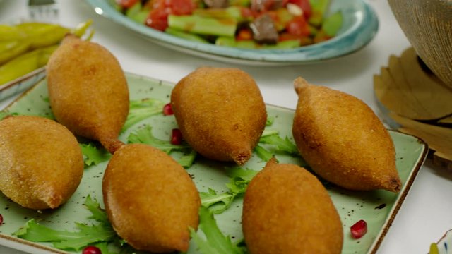 Delicious, fried traditional Mediterranean kibbeh garnished with pomegranate and salad on a plate.