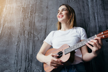 Attractive woman looking out the window and plays the ukulele. The setting sun shines on a beautiful woman.