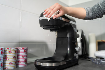 Close up on hands of unknown female caucasian person woman wiping cleaning stand mixer in the kitchen at home disinfection