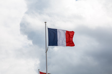 Flag of France against a blue sky with clouds.