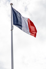 Flag of France against a blue sky with clouds.