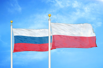 Russia and Poland two flags on flagpoles and blue cloudy sky