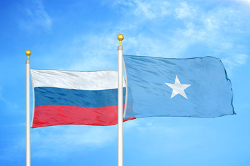 Russia and Somalia two flags on flagpoles and blue cloudy sky